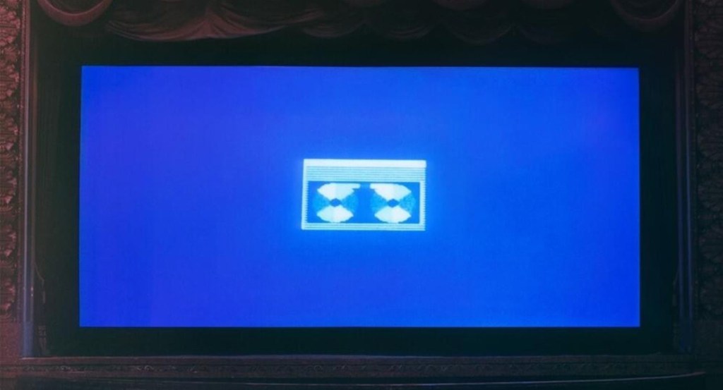 A cinema screen displaying a grainy VHS tape icon on a blue background